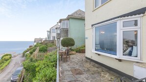 A coastal residential area with houses, a stone pathway, and a view of the sea. - 2 Bed in Looe (oc-l30026) (Looe)