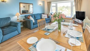 A dining area with a wooden table set for four, blue sofas, a mirror, and a TV. - 2 Bed in Looe (oc-l30026) (Looe)