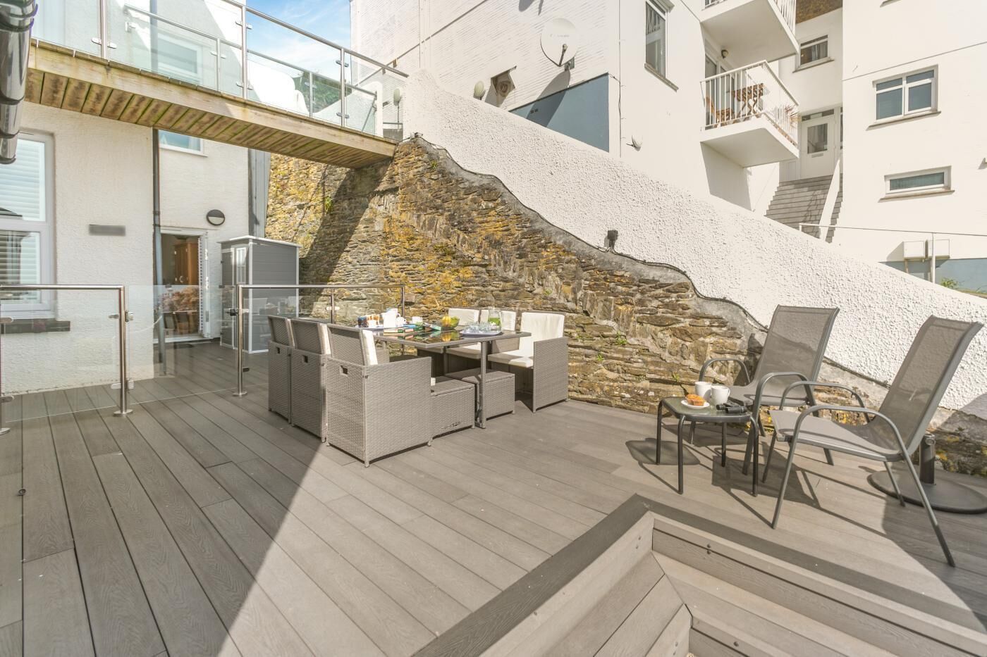 An outdoor patio with wicker furniture, a table with a cup and saucer, and a stone wall.