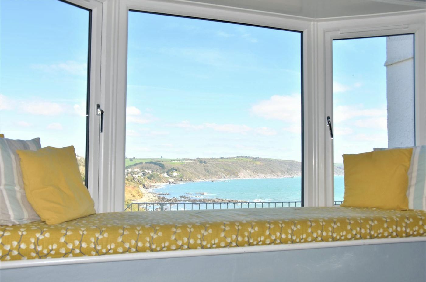 A room with a bed facing a large window overlooking a coastal landscape.