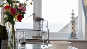 A table with a bottle of wine, a vase of flowers, a glass of water, and a bird perched on a glass. - 1 Bed in Looe (oc-l30008) (Looe)