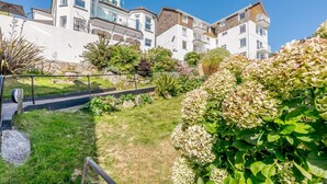 A residential building with multiple balconies, a well-maintained garden with hydrangeas, and a clear blue sky. - 1 Bed in Looe (oc-l30008) (Looe)
