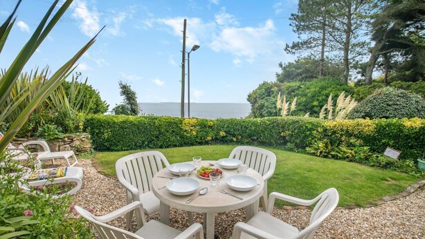 A round table with six white chairs, a small plate of fruit, and a glass of water. - 2 Bed in Looe (oc-l00055) (Trelawne)