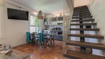 Una cocina moderna con electrodomésticos integrados, una zona de comedor con una mesa de vidrio y una escalera con escalones de madera.