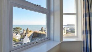 Een kamer met een groot raam met uitzicht op de kust, inclusief huizen en de zee.
