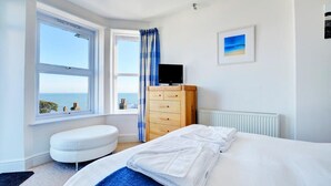 Een slaapkamer met een bed, een kaptafel, een televisie en uitzicht op zee.