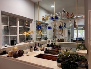 Une salle de bain moderne avec un grand miroir, un lavabo et des étagères où sont rangés des articles de toilette et de la verrerie.