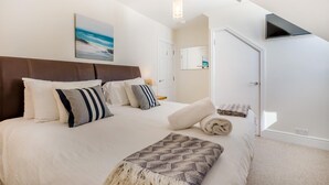 A bedroom with a bed, pillows, a blanket, a wall-mounted TV, a door, and a painting of a beach scene. - 2 Bed in Looe (oc-l30011) (Looe)