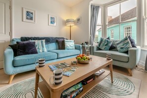 A living room with two light blue sofas, a coffee table with magazines and a bowl of fruit, and a Scrabble game set. - 4 Bed in Fowey (oc-chview) (Fowey)