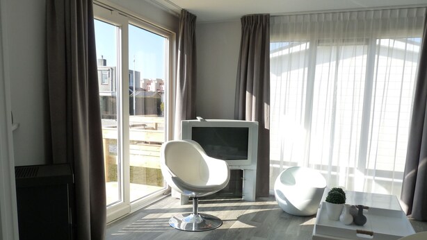 Een moderne woonkamer met een flatscreen televisie, een witte stoel en een kleine tafel met een plant.