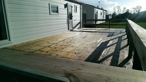 Een houten terras dat leidt naar een wit gebouw met een deur en ramen.
