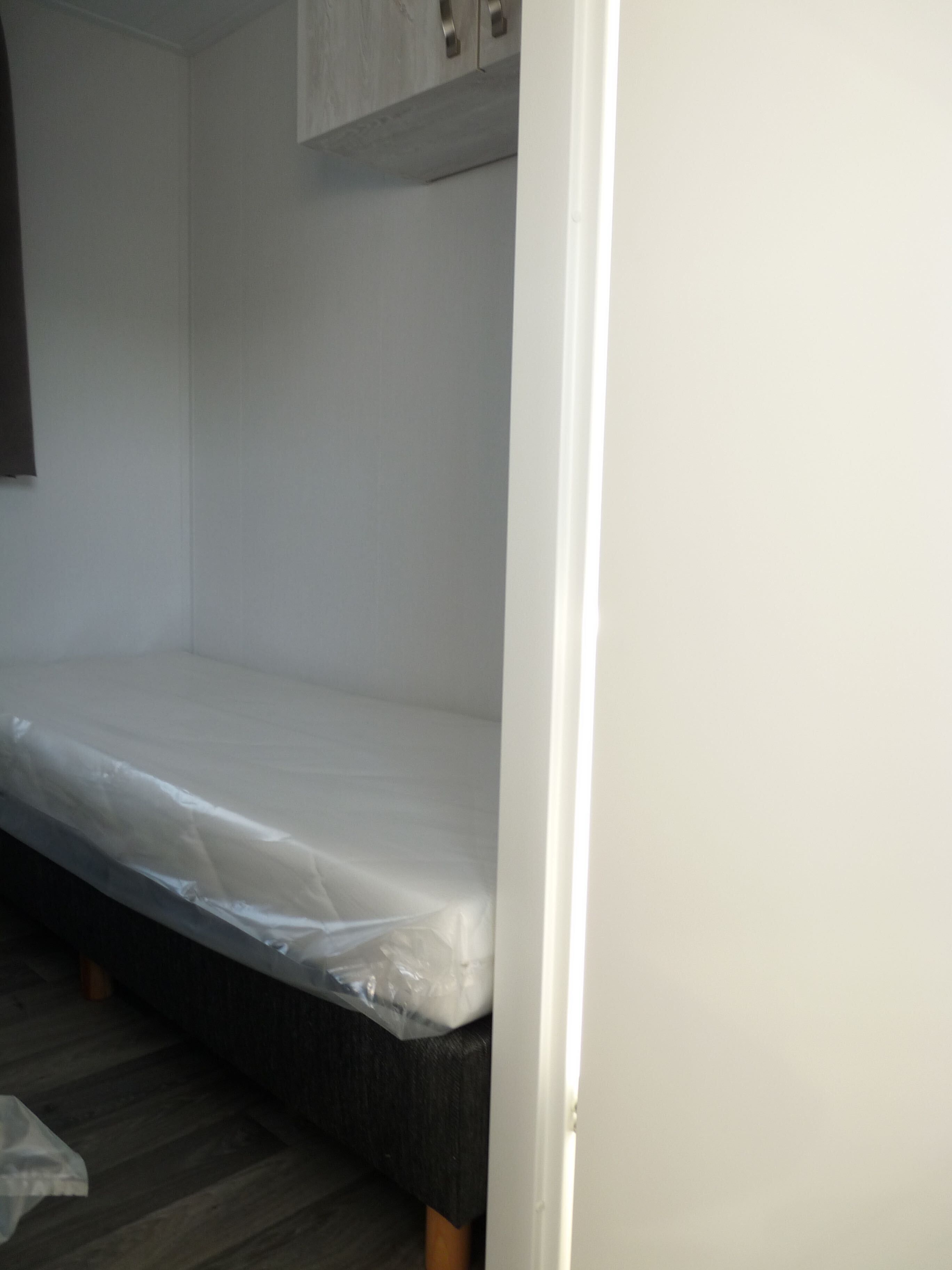 A bunk bed with a mattress covered in plastic, a wooden floor, and a white wall with a door frame.