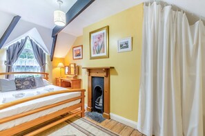 Um quarto com cama, lareira, janela com cortinas e uma parede com quadros.