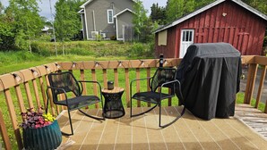 A covered outdoor deck with two rocking chairs, a small table, and a potted plant.