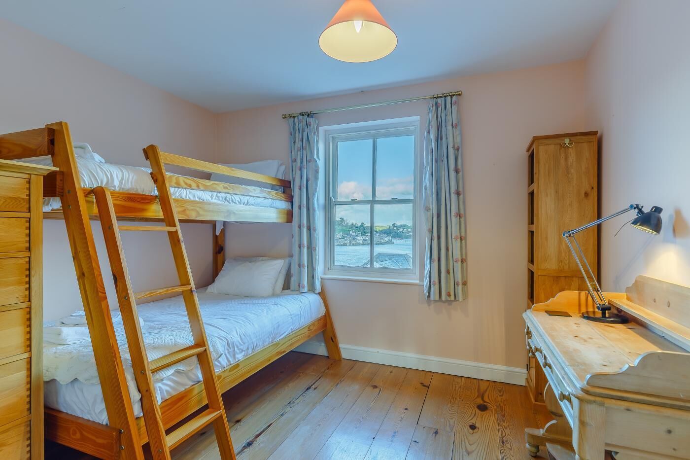 A bunk bed room with a window, a desk with a lamp, and a wardrobe.