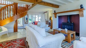 A spacious living room with a wooden staircase, a fireplace, and a large window offering a view of the outdoors. - 5 Bed in Polruan (oc-ccmead) (Fowey)