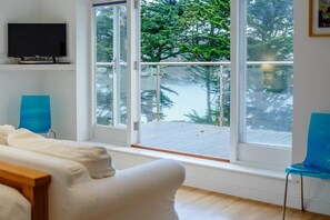 Een kamer met een groot raam dat uitkijkt op een besneeuwde veranda en bomen, een witte bank en twee blauwe stoelen.