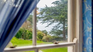 A window with a view of a lush garden and a large tree. - 5 Bed in Polruan (oc-ccmead) (Fowey)