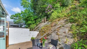 Patio esterno con tavolo e sedie rotonde, circondato da un muro bianco e da un pendio roccioso con vegetazione.
