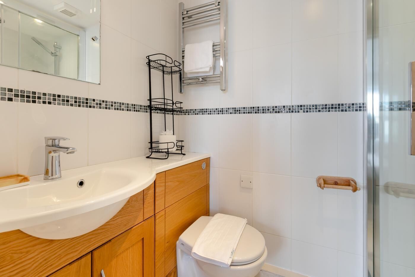 Une salle de bain moderne avec un lavabo blanc, un meuble-lavabo en bois, des toilettes et un espace douche.
