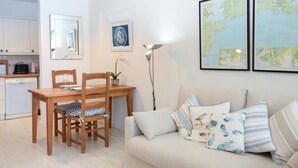 Una sala de estar con un sofá, una mesa de comedor con sillas, una lámpara, un mapa en la pared y una cocina al fondo.