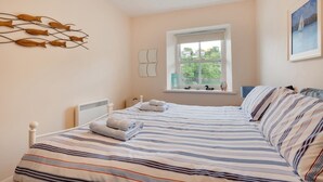 Un dormitorio con una cama grande, una ventana con vistas a la vegetación, un radiador y una obra de arte colgada en la pared.