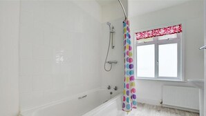 A bathroom with a white bathtub, a shower, and a window with a red valance. - 3 Bed in Fowey (oc-clenti) (Fowey)