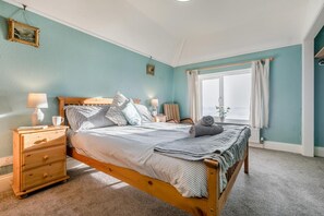 Ein Schlafzimmer mit einem hölzernen Bett, zwei Nachttischen, einem Fenster mit Vorhängen und Meerblick.