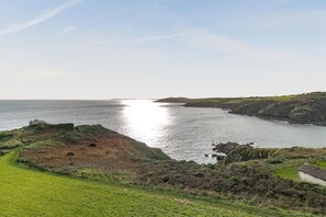 Eine Küstenlandschaft mit einer grasbewachsenen Fläche, Felsen und Blick auf das Meer.