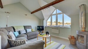 A loft-style living room with a sofa, TV, fireplace, and large windows offering a view. - 2 Bed in Fowey (oc-ccgree) (Fowey)