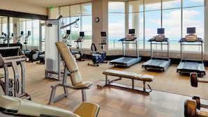 A gym with exercise equipment, large windows, and a view of the beach.