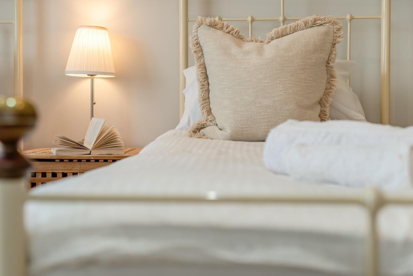 A neatly made bed with a pillow, a bedside lamp, and an open book on a wooden nightstand.