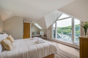 A bedroom with a large bed, a skylight, a view of a balcony, and a wooden dresser. - 4 Bed in Looe (oc-l30016) (Looe)