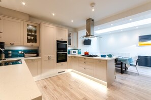 A modern kitchen with built-in appliances, a dining area with a table and chairs, and a view of the outdoors. - 4 Bed in Looe (oc-l30016) (Looe)