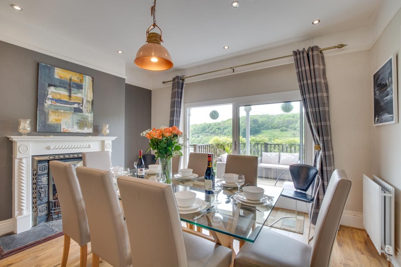 A dining area with a glass table, chairs, a vase with flowers, and a view of the outdoors.