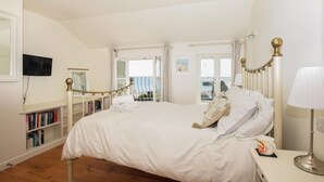 Et soveværelse med en stor seng, et sengebord med en lampe, en bogreol og havudsigt gennem et vindue.