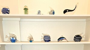 A corner shelving unit with various glass and ceramic objects. - Retro Vibes-2 BR/2 Bath Cottage, Big Deck, Boat Parking, Beach Nearby, Dogs OK! (Port Aransas)