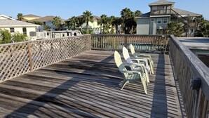 A wooden deck with Adirondack chairs, a wooden fence, and houses in the background. - Retro Vibes-2 BR/2 Bath Cottage, Big Deck, Boat Parking, Beach Nearby, Dogs OK! (Port Aransas)
