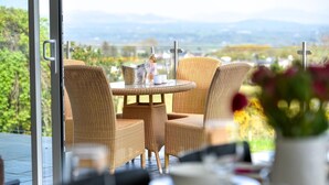 A dining area with wicker chairs and a round table, overlooking a scenic landscape. - 5 Bed in Pwllheli (oc-dolwen) (Llanbedrog)