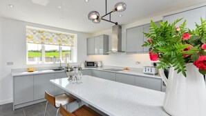 A modern kitchen with a central island, grey cabinetry, and a large window with a view. - 5 Bed in Pwllheli (oc-dolwen) (Llanbedrog)