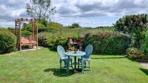 A garden with a wooden pergola, a round table with chairs, and a brick planter with plants. - 2 Bed in Pwllheli (oc-wag303) (Y Ffôr)