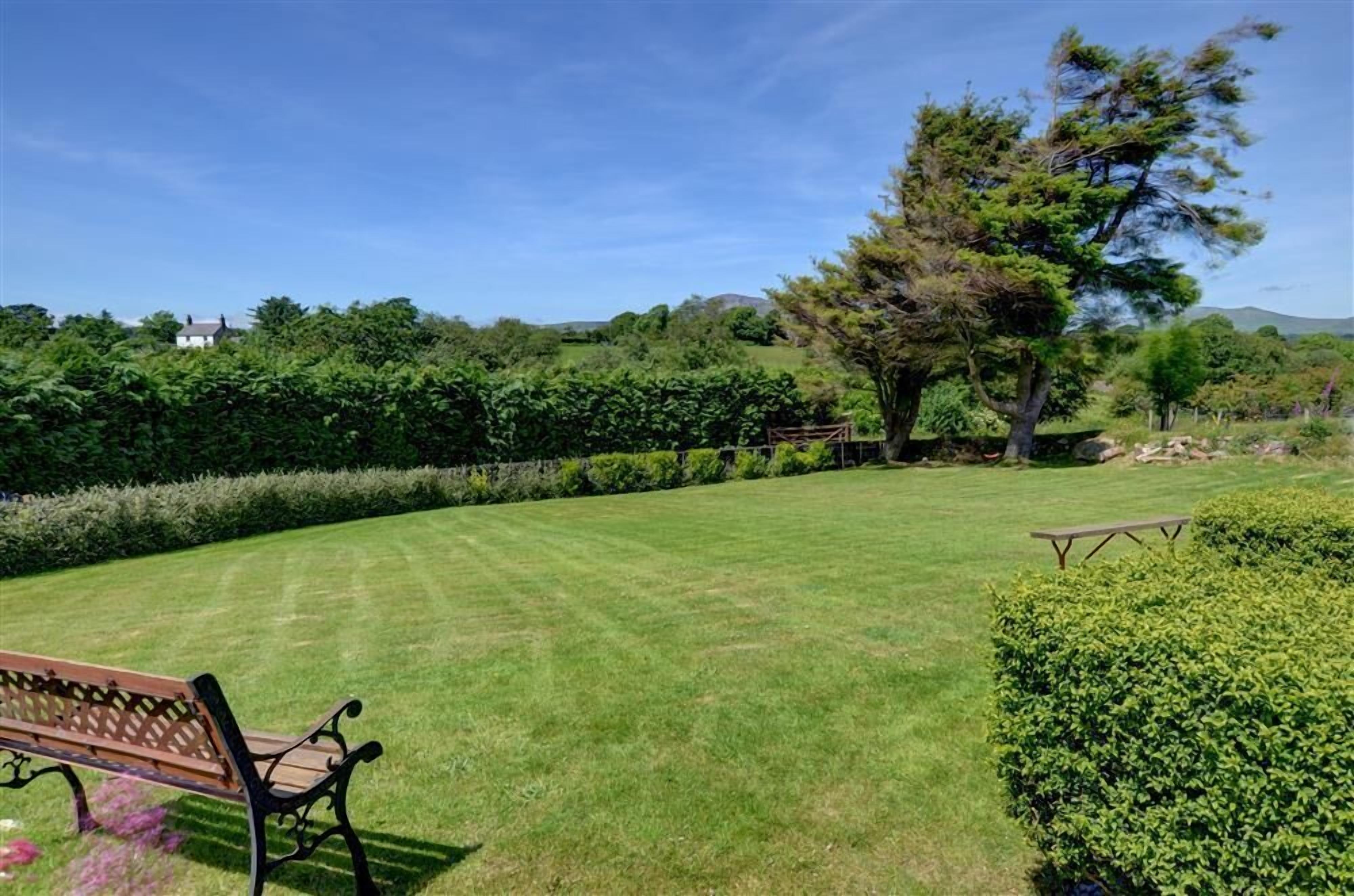 Een verzorgd gazon met een houten bank en een picknicktafel, omringd door dichte hagen en bomen.