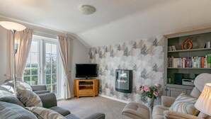 A living room with a sofa, armchair, TV, bookshelf, and a decorative vase. - 2 Bed in Pwllheli (oc-wag303) (Y Ffôr)