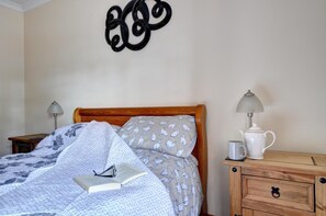 A neatly made bed with a patterned blanket, a bedside lamp, and a bedside table with a mug and a book. - 2 Bed in Y Felinheli (oc-wag431) (Y Felinheli)
