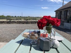 A picnic setup on a green table with food items, a vase of red flowers, and a sugar container. - 2 Bed in Y Felinheli (oc-wag431) (Y Felinheli)