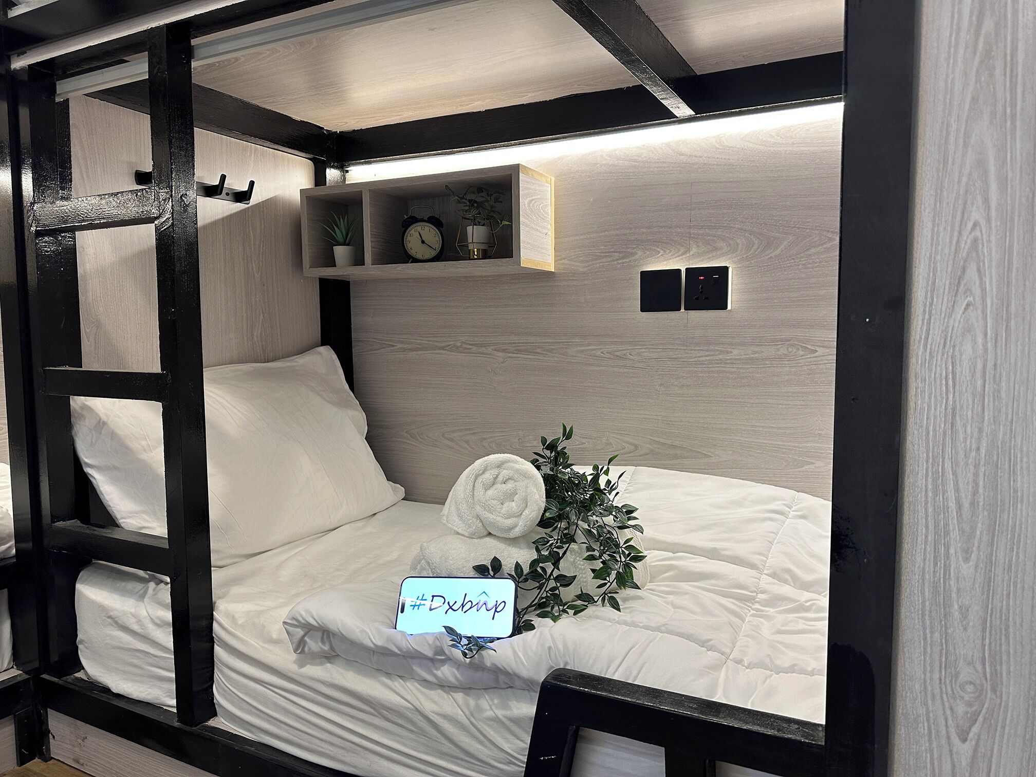 A bunk bed with a wooden headboard, a small shelf with a clock and a plant, and a sign with a hashtag.