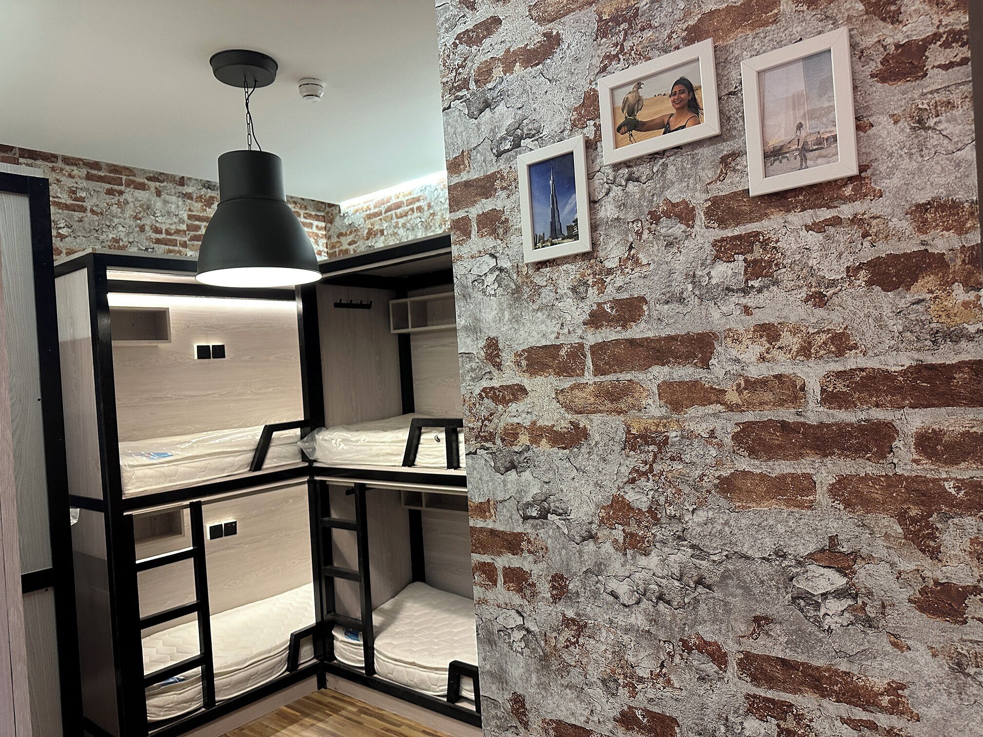 A room with a loft bed, a hanging light fixture, and a brick wall with framed pictures.