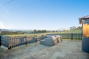 A patio with stone flooring, a wooden fence, and a seating area with cushions. - 3 Bed in Pwllheli (oc-brynre) (Mynytho)