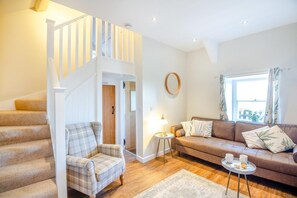 Eine Treppe führt zu einem Schlafzimmer auf dem Dachboden, ein Wohnzimmer mit Sofa und Couchtisch sowie ein Fenster mit Vorhängen.