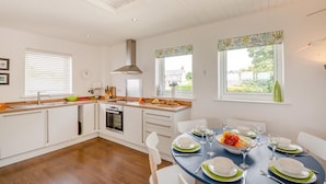 A modern kitchen with white cabinetry, a central island, and a dining area set for four. - 3 Bed in Abersoch (oc-4ynysf) (Abersoch)